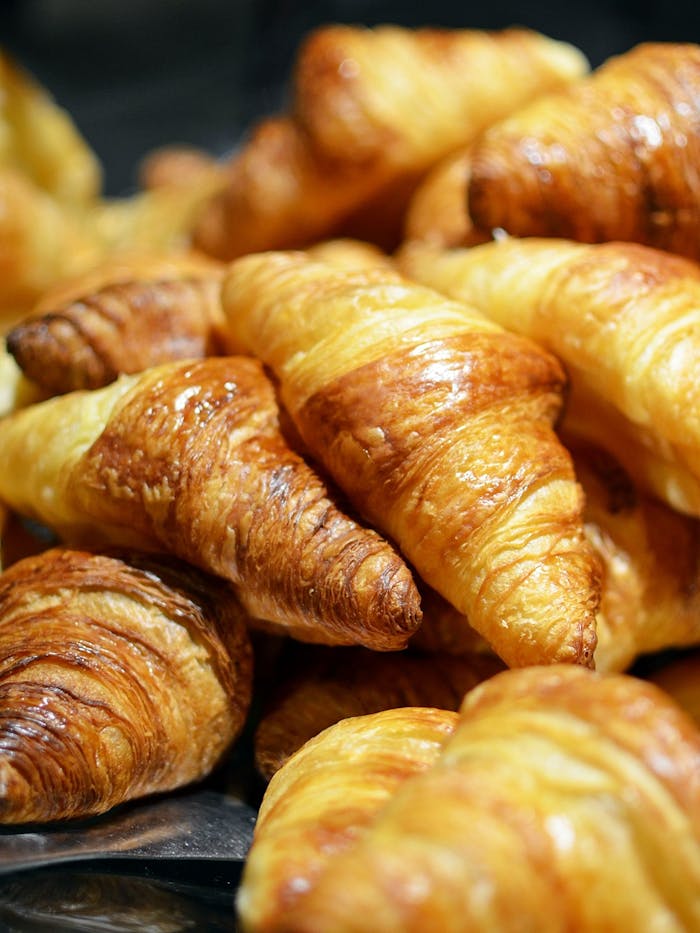 about-01 A stack of golden, freshly baked croissants showcasing flaky layers in a bakery setting.