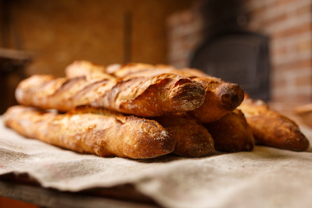 hero-img-01 Warm, freshly baked rustic baguettes stacked in a cozy bakery setting.